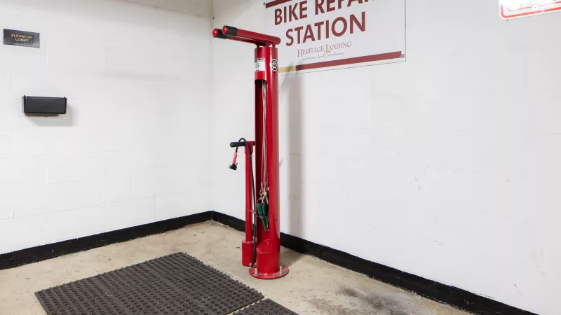Red public bike repair station with various tools, in a white room with a dark mat.