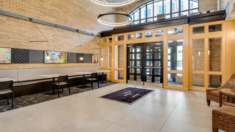 Elegant lobby with exposed brick walls, modern circular lights, arched glass entrance, and a long bench seating area.