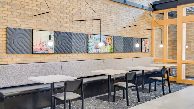 Modern cafe with exposed brick, long grey banquette, light tables, and abstract art panels along the wall.