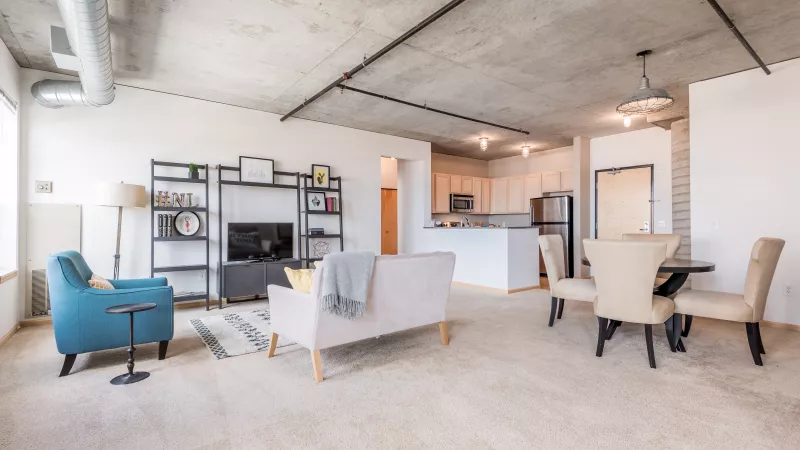 modern open-concept apartment featuring a living room with teal armchair, pink sofa, dining area, and kitchen.