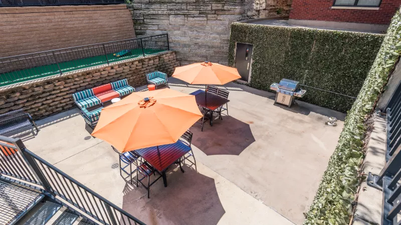 Outdoor patio with orange umbrellas, seating, and grills. Surrounded by brick, stone, and ivy walls.