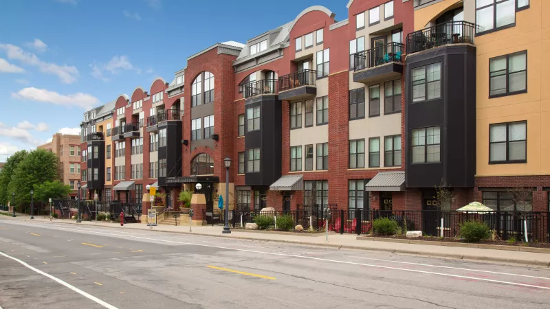 Modern brick apartment buildings with diverse facades and balconies line a street under a clear blue sky.