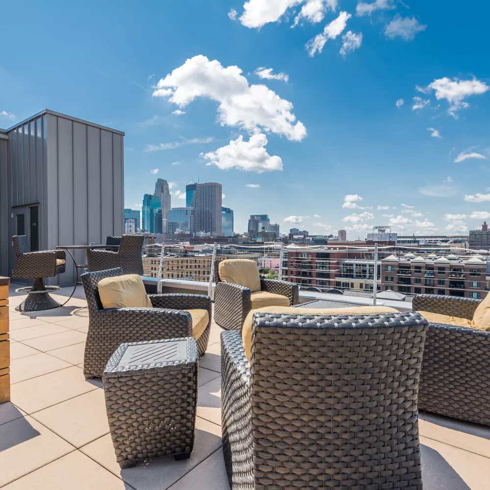 Rooftop patio with wicker furniture, yellow cushions, city skyline, and blue sky.