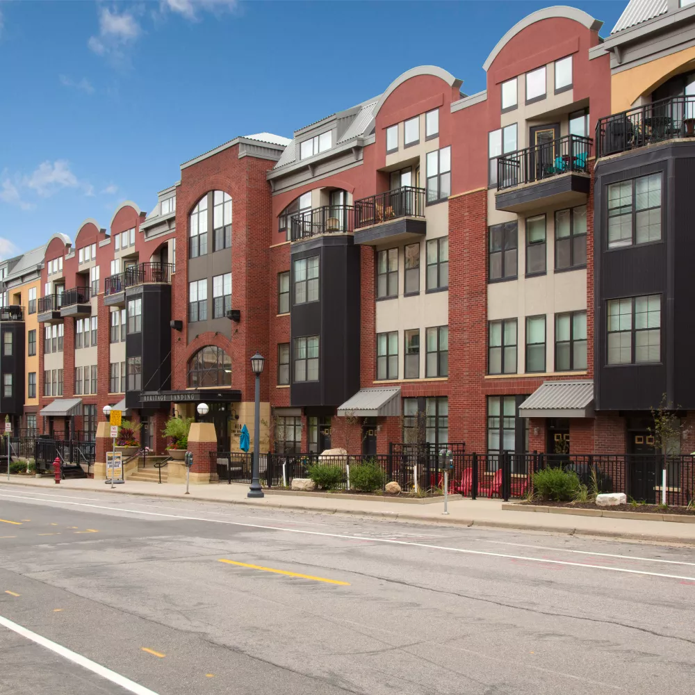 Modern brick apartment buildings with diverse facades and balconies line a street under a clear blue sky.