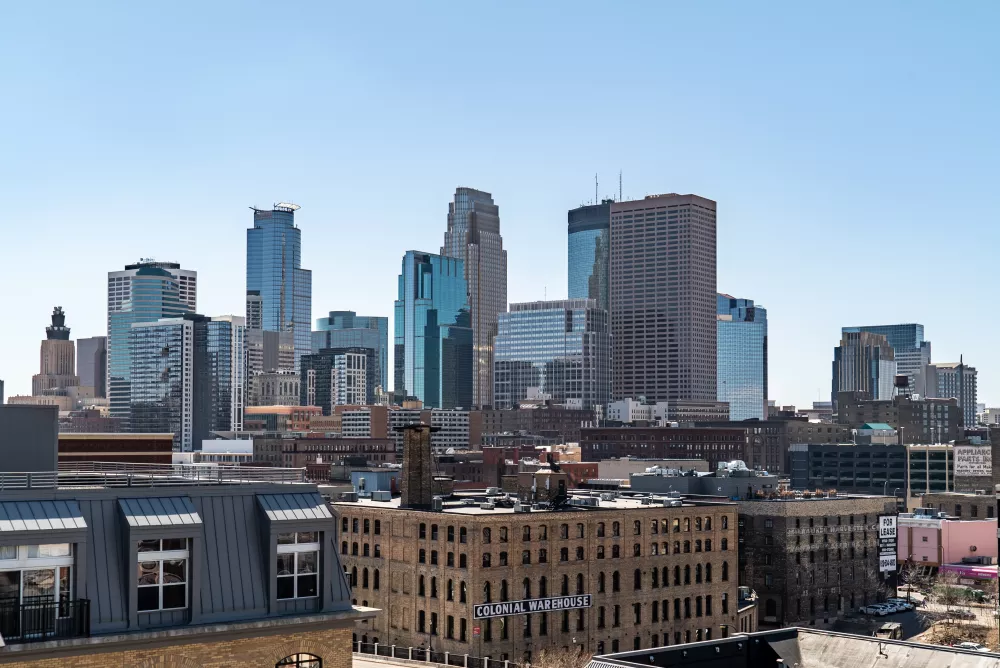 Daytime city skyline with a mix of modern glass skyscrapers and older brick buildings under a clear blue sky. Photograph.