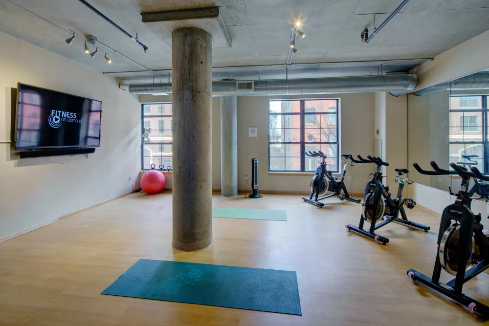 Modern gym with exercise bikes, yoga mats, a TV, and a red exercise ball. Concrete pillar in the center.